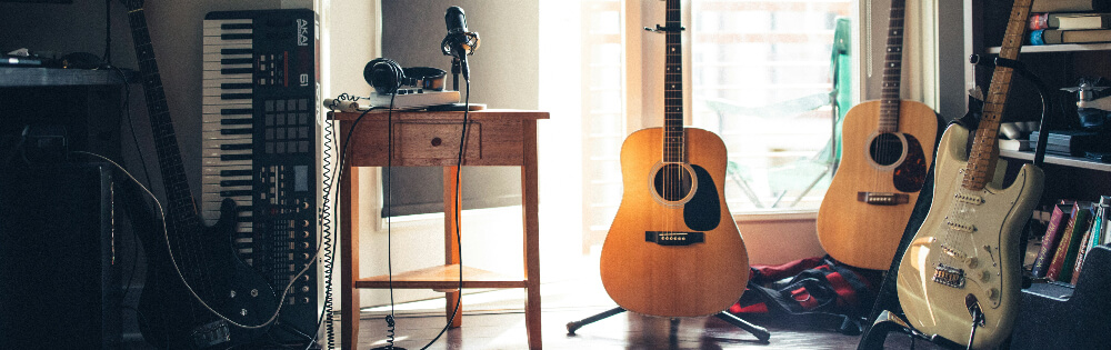 Musikinstrumente Raum mit Musikinstrumenten, darunter ein Keyboard, ein Tisch mit Kopfhörern und einem Mikrofon, zwei Akustikgitarren und eine E-Gitarre.